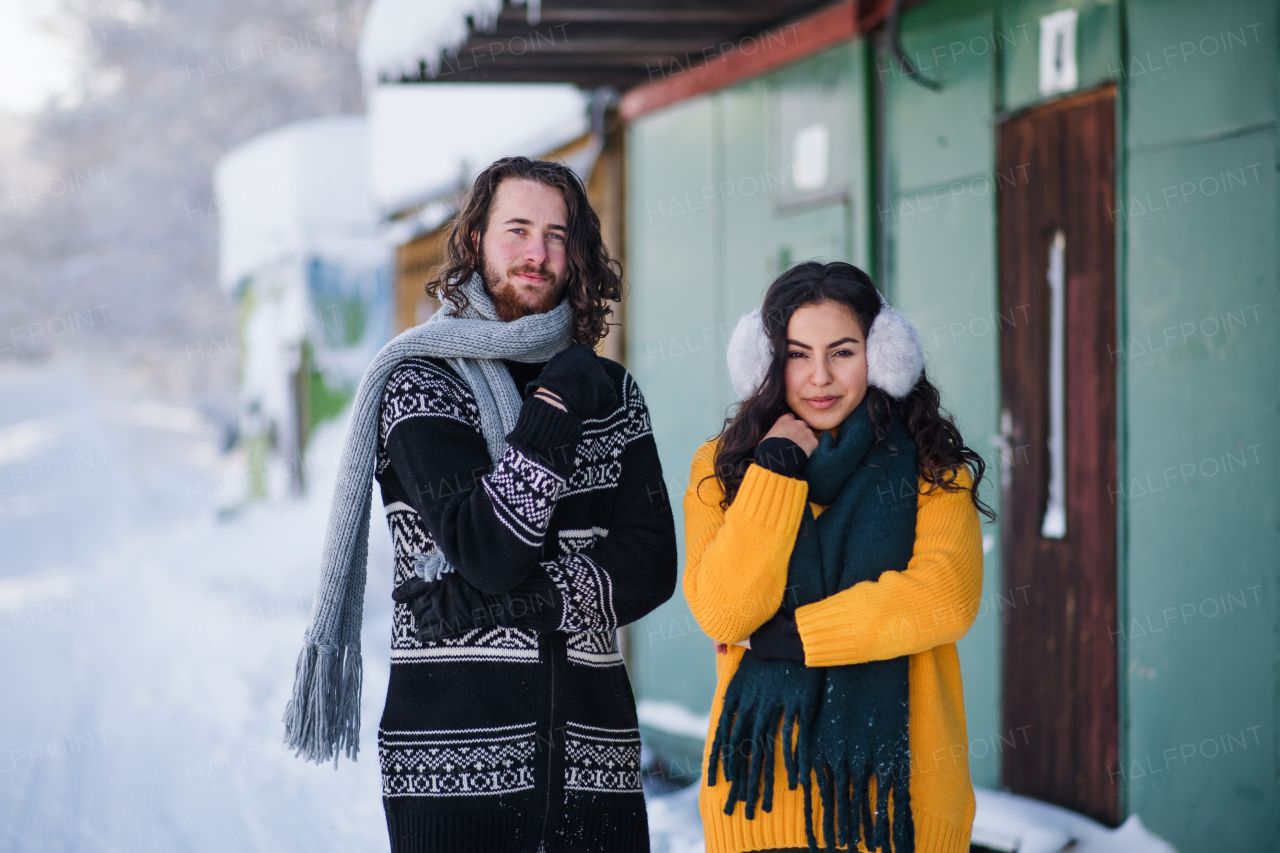 A portrait of young couple standing outdoors in winter, looking at camera.