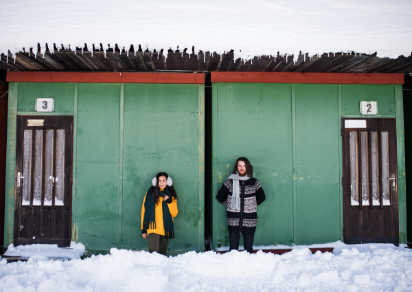 A portrait of young couple standing outdoors in winter, looking at camera.