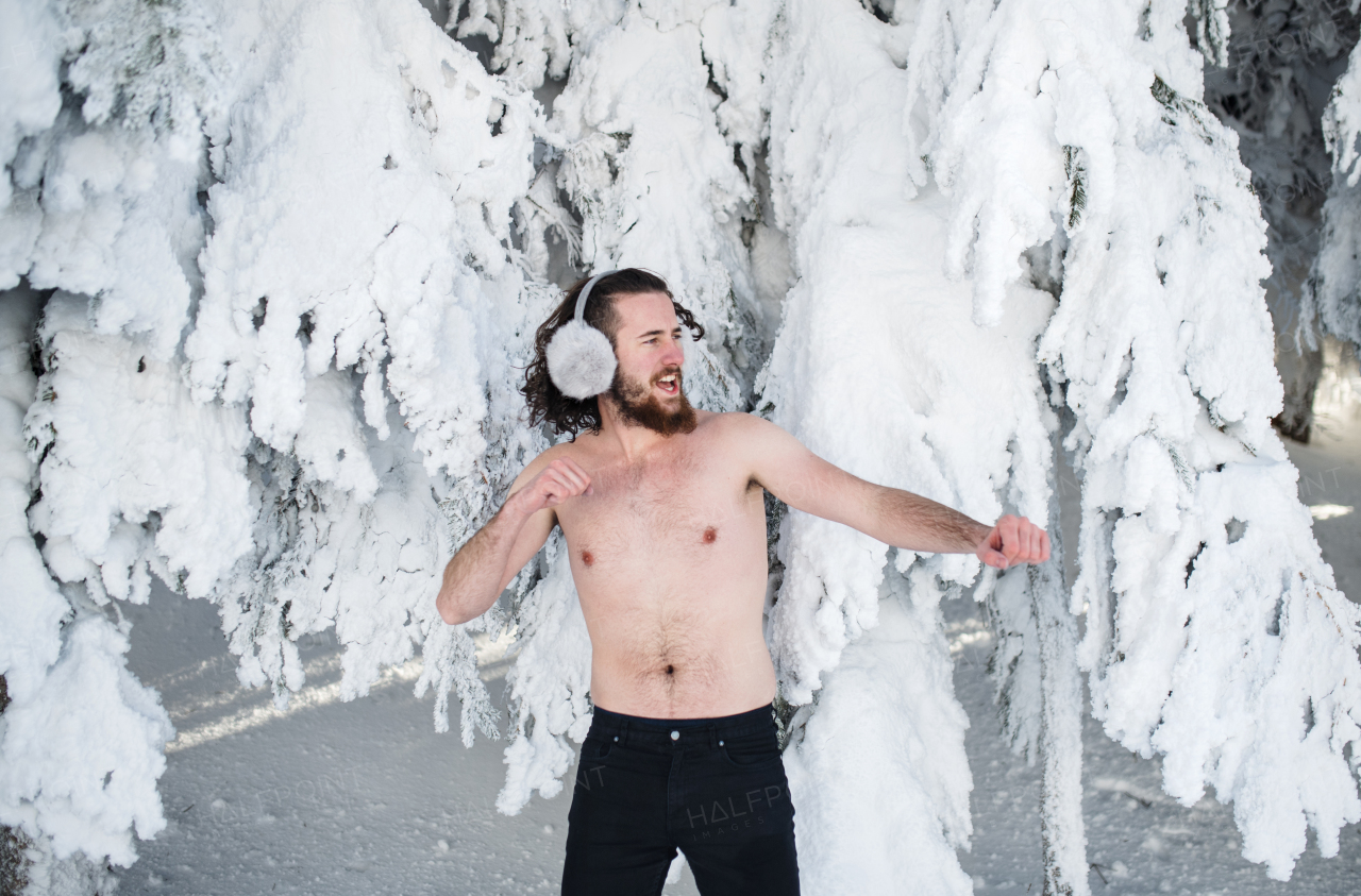 A portrait of topless young man outdoors in snow in winter forest, having fun.