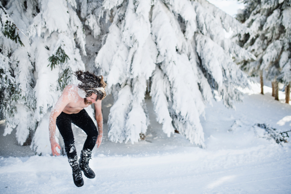 A portrait of topless young man outdoors in snow in winter forest, having fun.