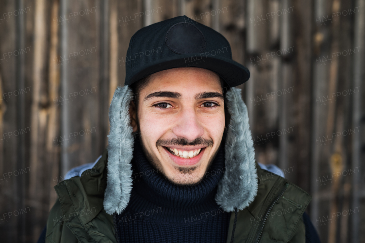 Front view portrait of young man standing against wooden background outdoors in winter.