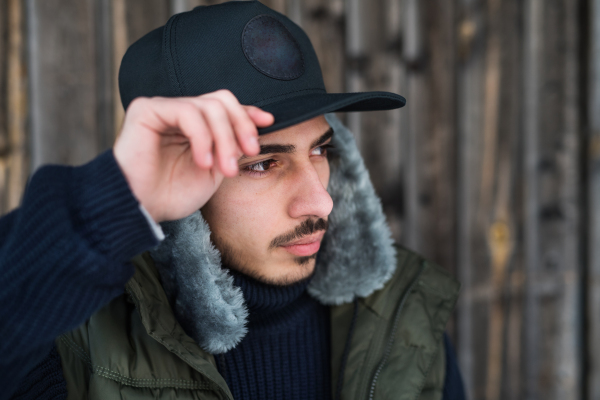 Front view portrait of young man standing against wooden background outdoors in winter.