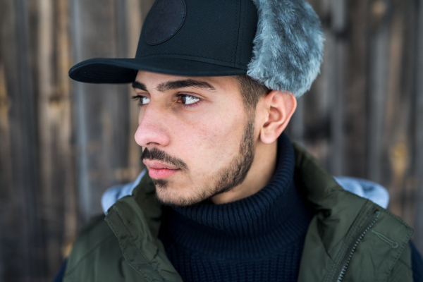 Front view portrait of young man standing against wooden background outdoors in winter, close-up.