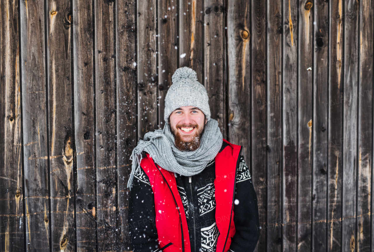 Front view portrait of young man standing against wooden background outdoors in winter.