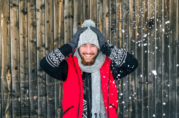 Front view portrait of young man standing against wooden background outdoors in winter.