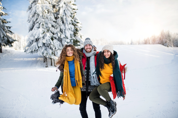 A group of cheerful young cheerful friends standing outdoors in snow in winter forest, having fun.