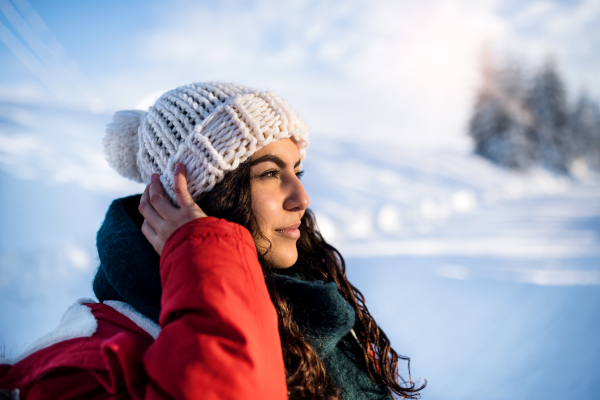 A front view portrait of young woman standing outdoors in snowy winter forest, wearing woollen hat.