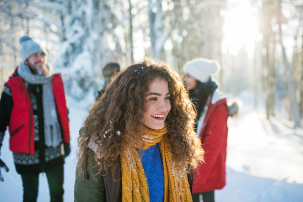 A portrait of young cheerful woman with friends standing outdoors in snowy winter forest.