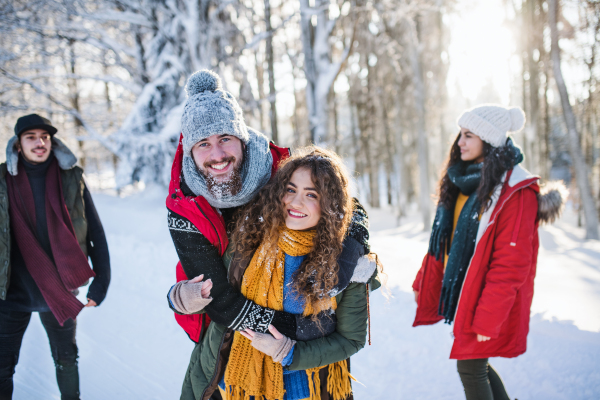 A group of young cheerful friends on a walk outdoors in snow in winter forest, having fun.