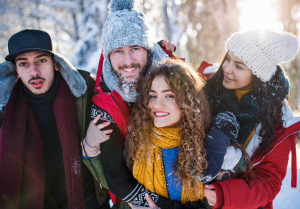 A group of young cheerful friends on a walk outdoors in snow in winter forest, looking at camera.