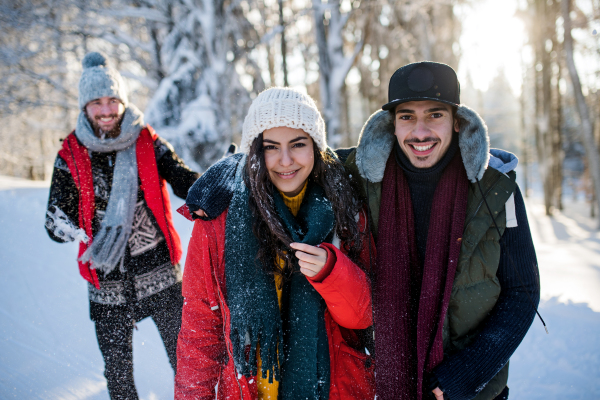 A group of young cheerful friends on a walk outdoors in snow in winter forest, having fun.