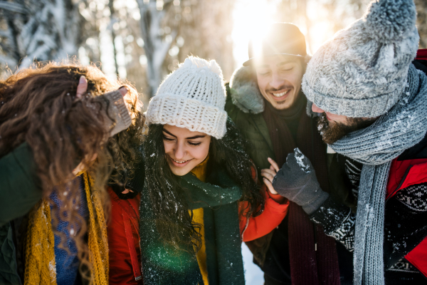 A group of young cheerful friends on a walk outdoors in snow in winter forest, having fun.