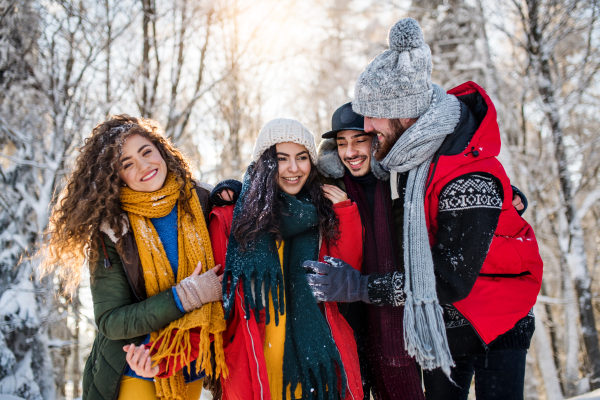 A group of young cheerful friends on a walk outdoors in snow in winter forest, walking.