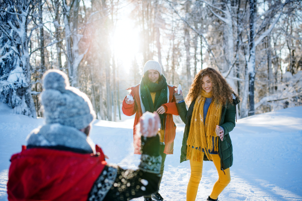 A group of young cheerful friends on a walk outdoors in snow in winter forest, having fun.