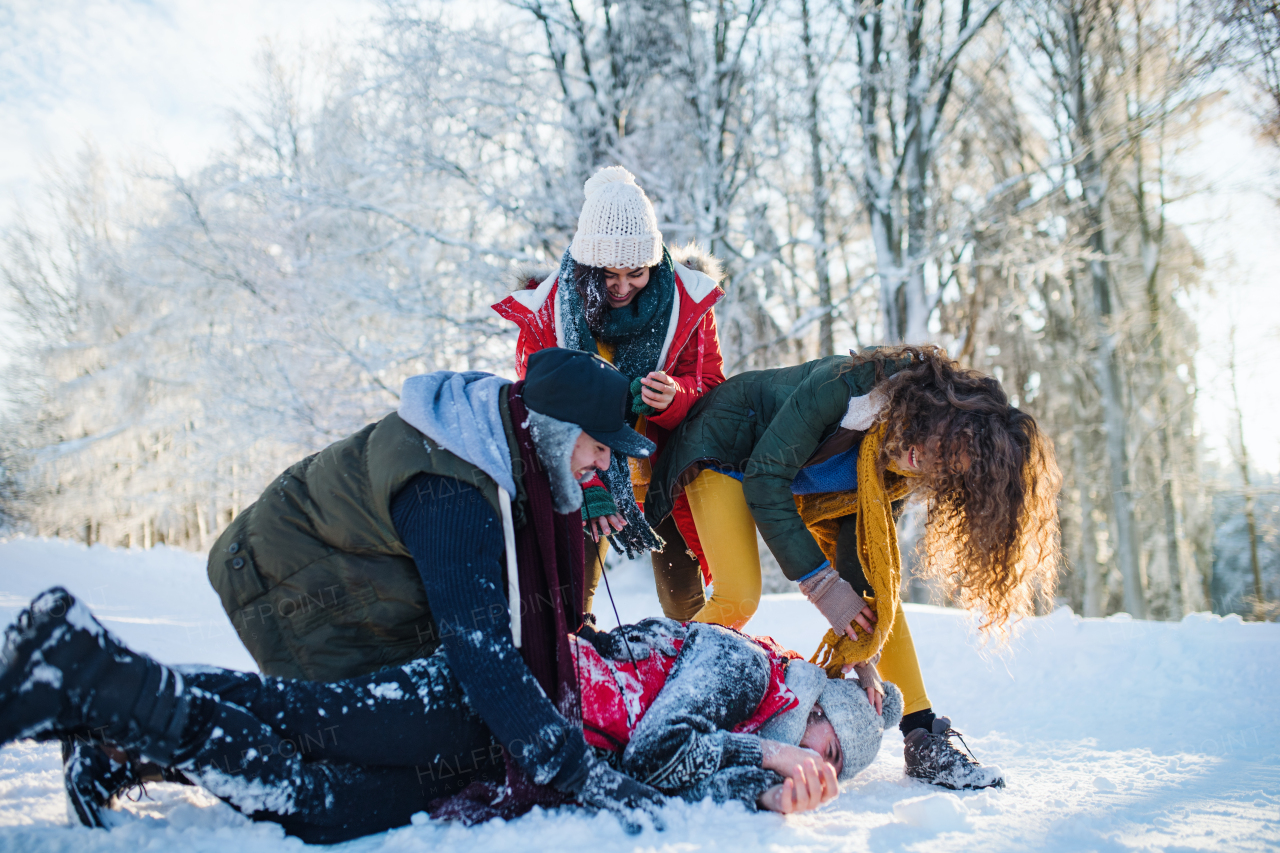 A group of young cheerful friends on a walk outdoors in snow in winter forest, having fun.