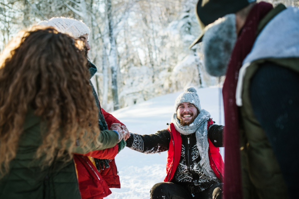 A group of young cheerful friends on a walk outdoors in snow in winter forest, having fun.