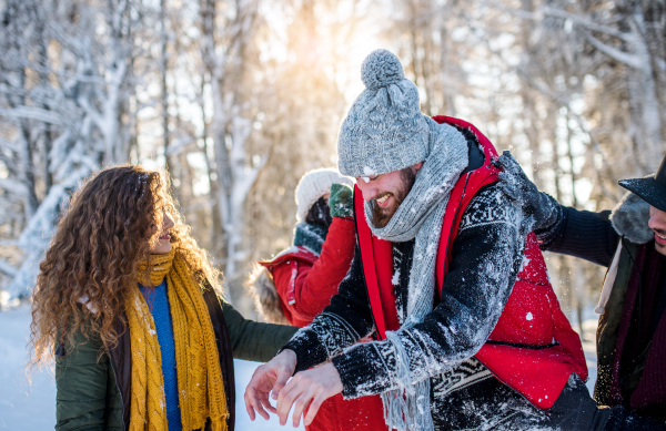 A group of young cheerful friends on a walk outdoors in snow in winter forest, having fun.