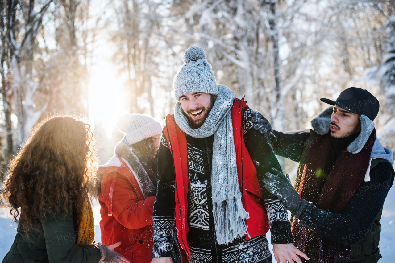 A group of young cheerful friends on a walk outdoors in snow in winter forest, having fun.