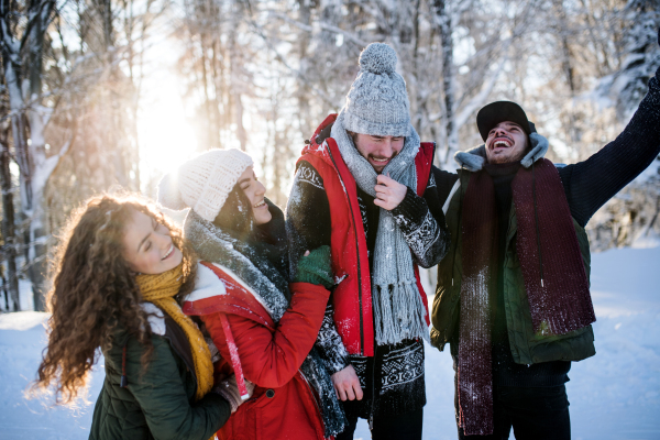 A group of young cheerful friends on a walk outdoors in snow in winter forest, having fun.