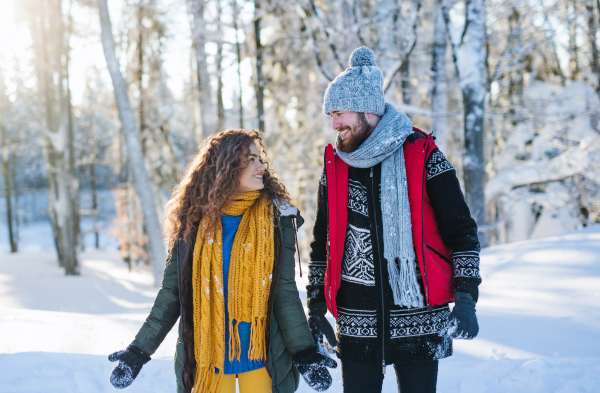 A portrait of couple walking outdoors in snow in winter forest, talking.