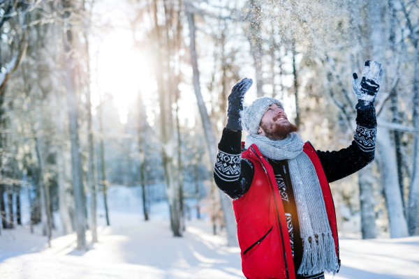 Cheerful young man having fun in snow outdoors in winter. Copy space.