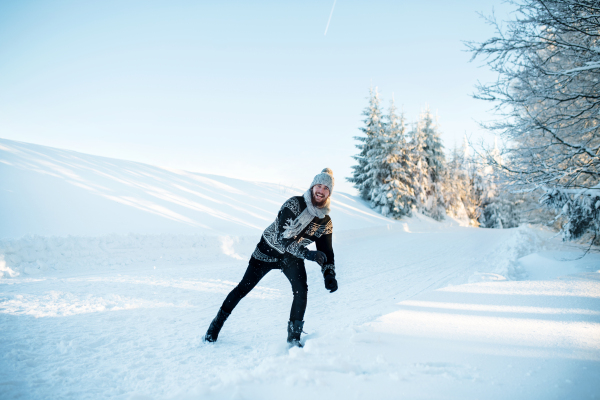 Cheerful young man having fun in snow outdoors in winter.