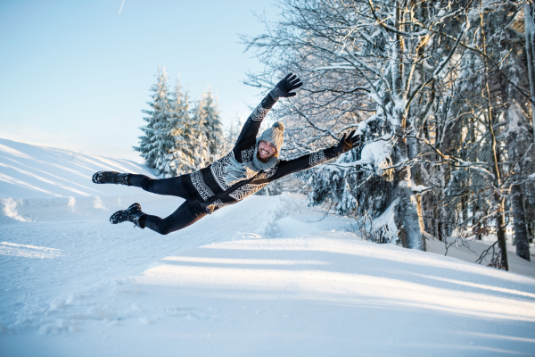 Young man having fun outdoors in winter, jumping in snow.