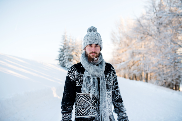 Portrait of young man standing in snow nature outdoors in winter, looking at camera.