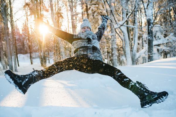 Young man having fun outdoors in winter, jumping in snow.