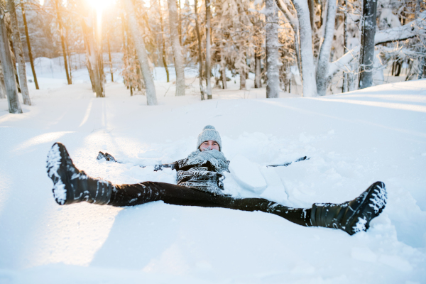 Young man having fun outdoors in winter, lying in snow.