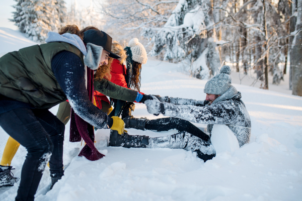 A group of young cheerful friends on a walk outdoors in snow in winter forest, having fun.