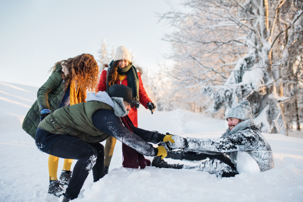 A group of young cheerful friends on a walk outdoors in snow in winter forest, having fun.