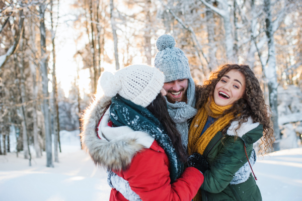 A group of cheerful young cheerful friends standing outdoors in snow in winter forest, having fun.