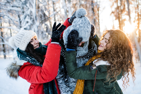 A group of cheerful young cheerful friends standing outdoors in snow in winter forest, having fun.