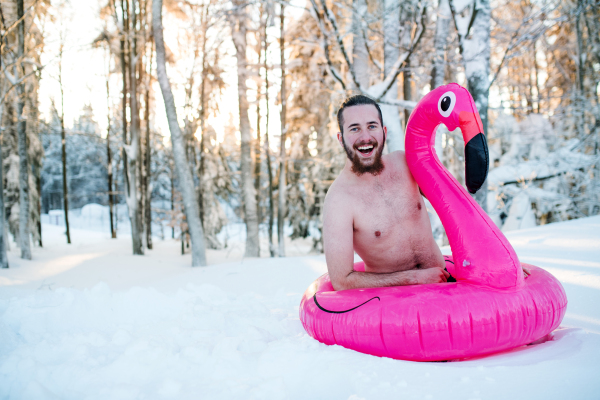 A portrait of topless young man outdoors in snow in winter forest, having fun.