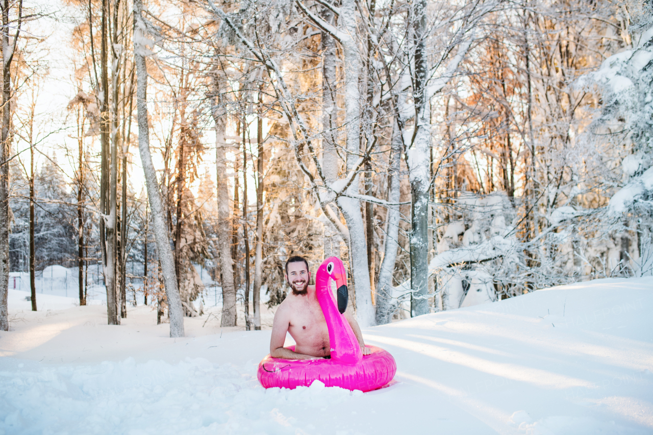 A portrait of topless young man outdoors in snow in winter forest, having fun.