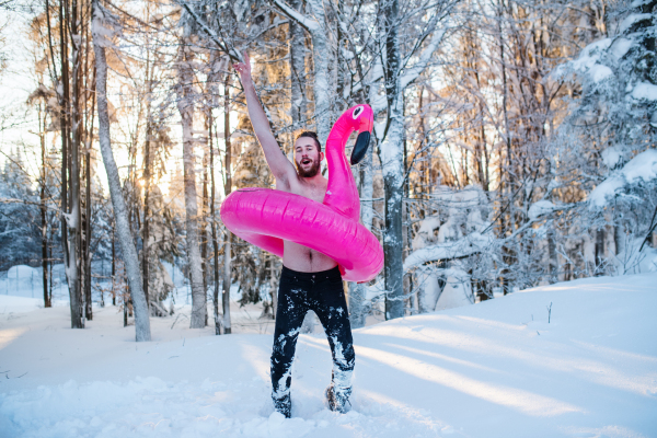 A portrait of topless young man outdoors in snow in winter forest, having fun.