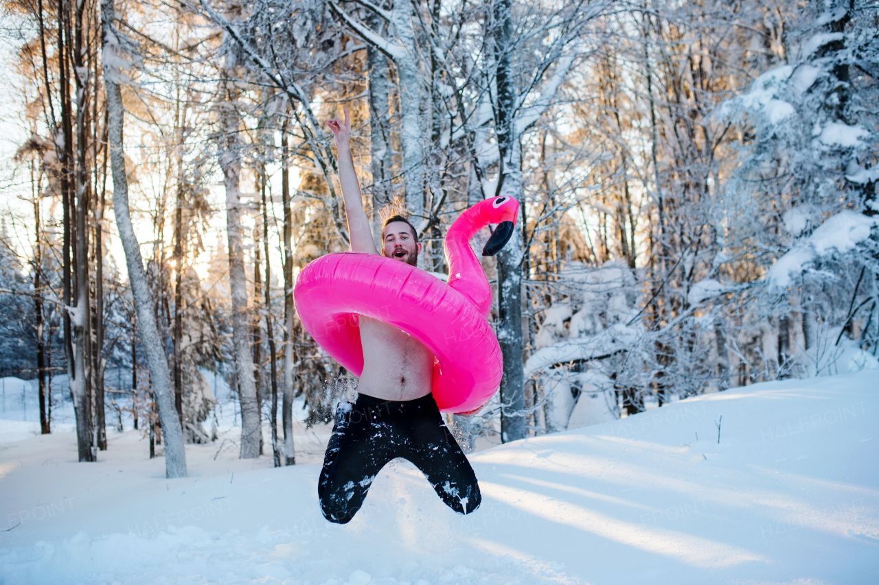 A portrait of topless young man outdoors in snow in winter forest, having fun.