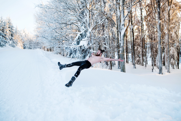 A portrait of topless young man outdoors in snow in winter forest, having fun.