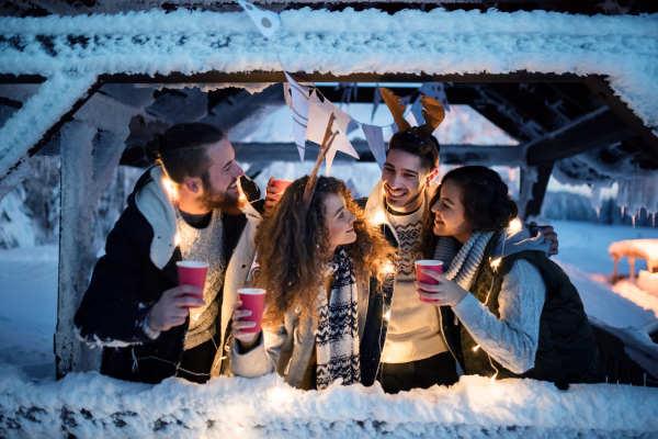 A group of young friends outdoors in snow in winter at night, holding drinks.