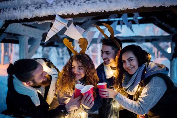 A group of young friends outdoors in snow in winter at night, holding drinks.