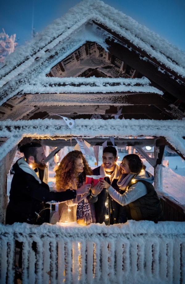 A group of young friends outdoors in snow in winter at night, holding drinks.