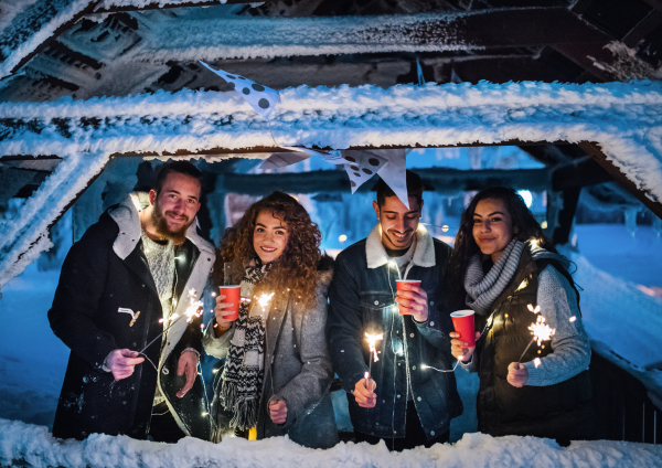 A group of young friends outdoors in snow in winter at night, holding sparklers.