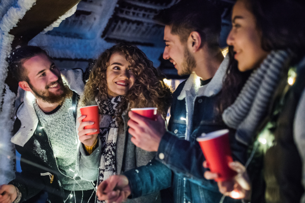 A group of young friends outdoors in snow in winter at night, holding sparklers.