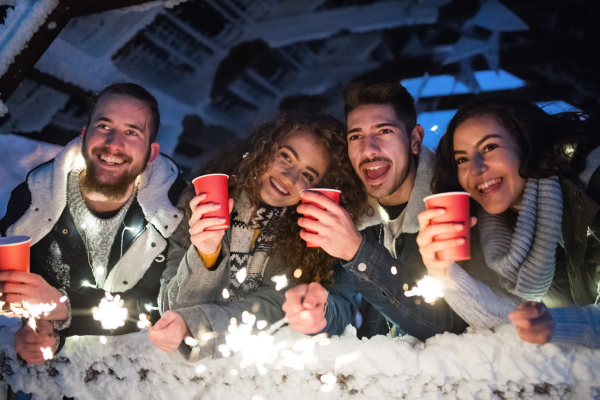 A group of young friends outdoors in snow in winter at night, holding drinks.