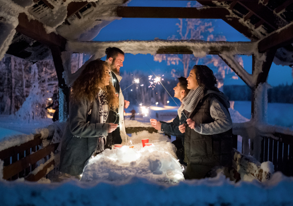 A group of young friends outdoors in snow in winter at night, holding sparklers.