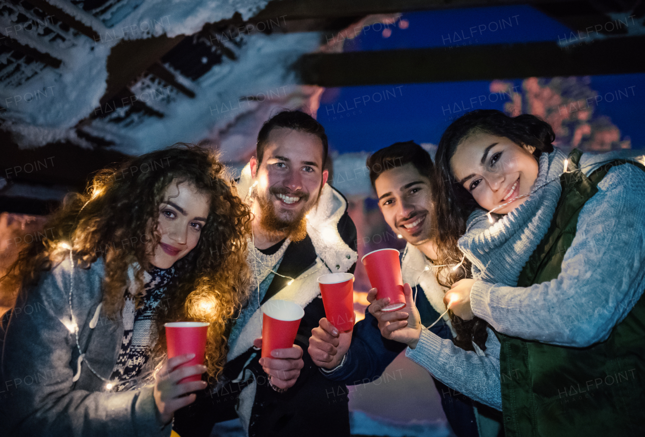 A group of young friends outdoors in snow in winter at night, holding drinks.