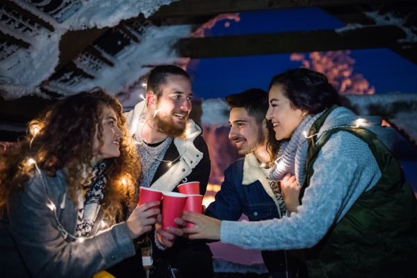 A group of young friends outdoors in snow in winter at night, holding sparklers.