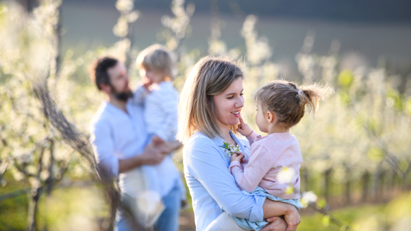 Front view of family with two small children standing outdoors in orchard in spring.