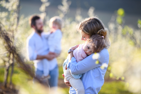 Front view of family with two small children standing outdoors in orchard in spring.